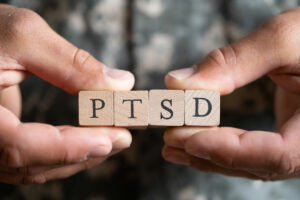 Two hands hold together 4 blocks each with a letter on them, the blocks spell out PTSD