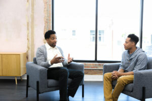 Young person of color sits in a room across an older person of color looking to be in an important discussion