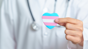 Healthcare professional holding a heart-shaped symbol in the colors of the transgender pride flag, representing support for transgender health, inclusion and affirming care.