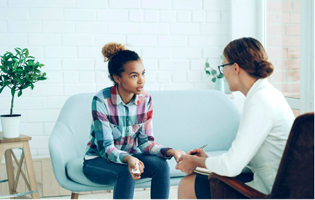 A therapist and a young adult sit facing each other in a counseling office, engaged in a supportive conversation.